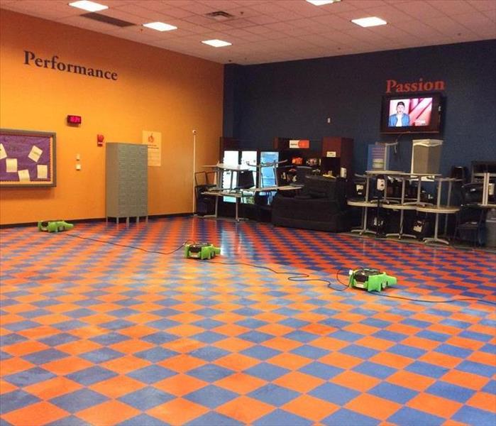 large room with dull, checkered orange and blue tile, green air movers on the floor